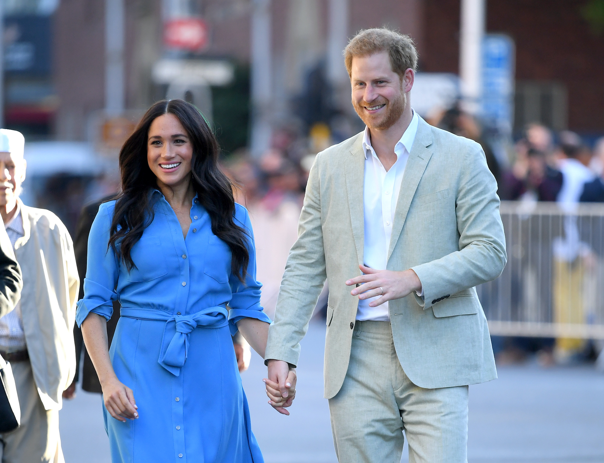 (L-R) Meghan Markle and Prince Harry smiling, walking down a street, holding hands