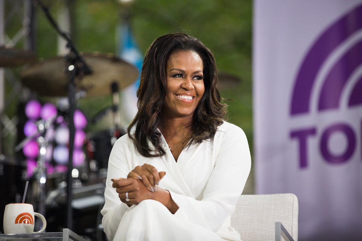 Michelle Obama smiling and looking to her right wearing a white blazer.