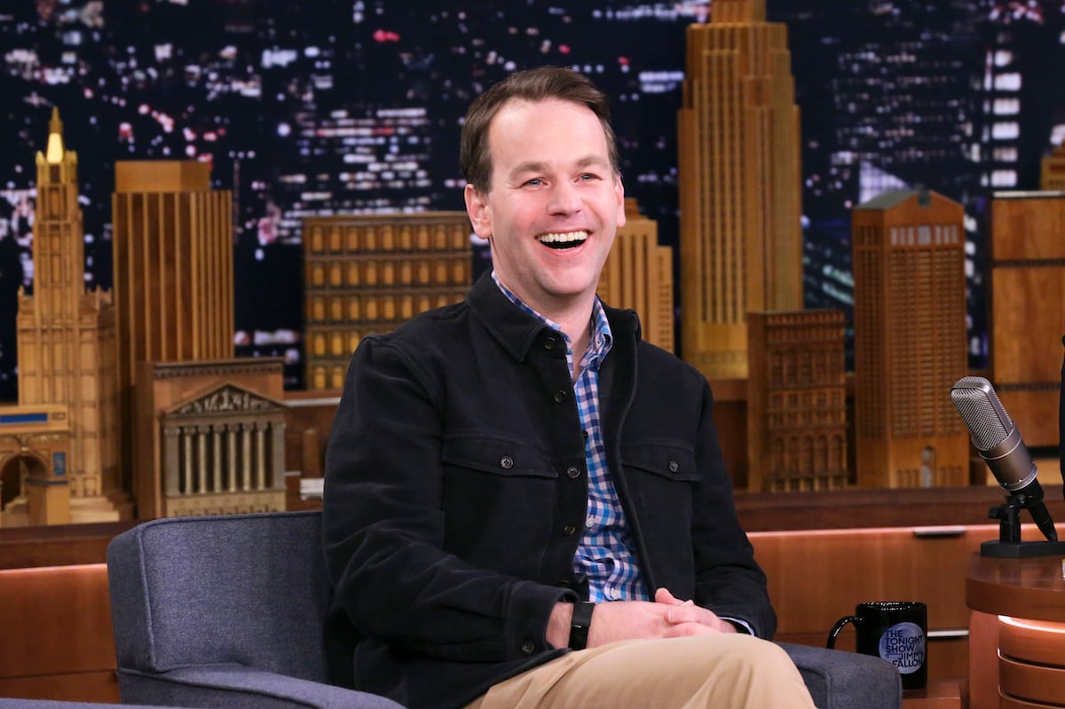 Mike Birbiglia sitting on a chair smiling at the audience