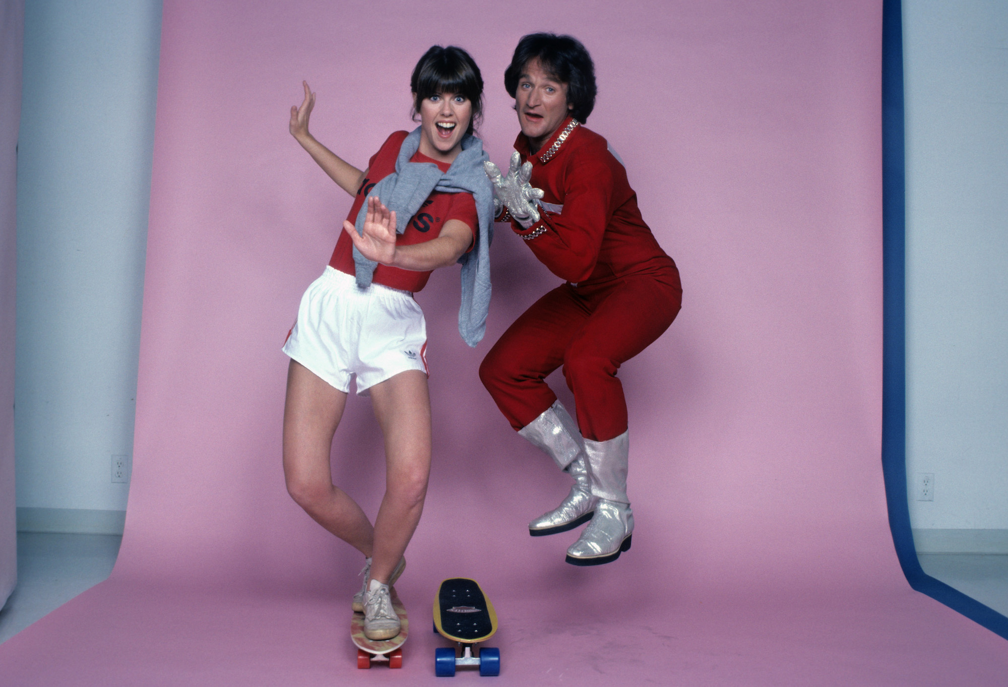 (L-R) Pam Dawber as Mindy McConnell and Robin Williams as Mork smiling in front of a pink background