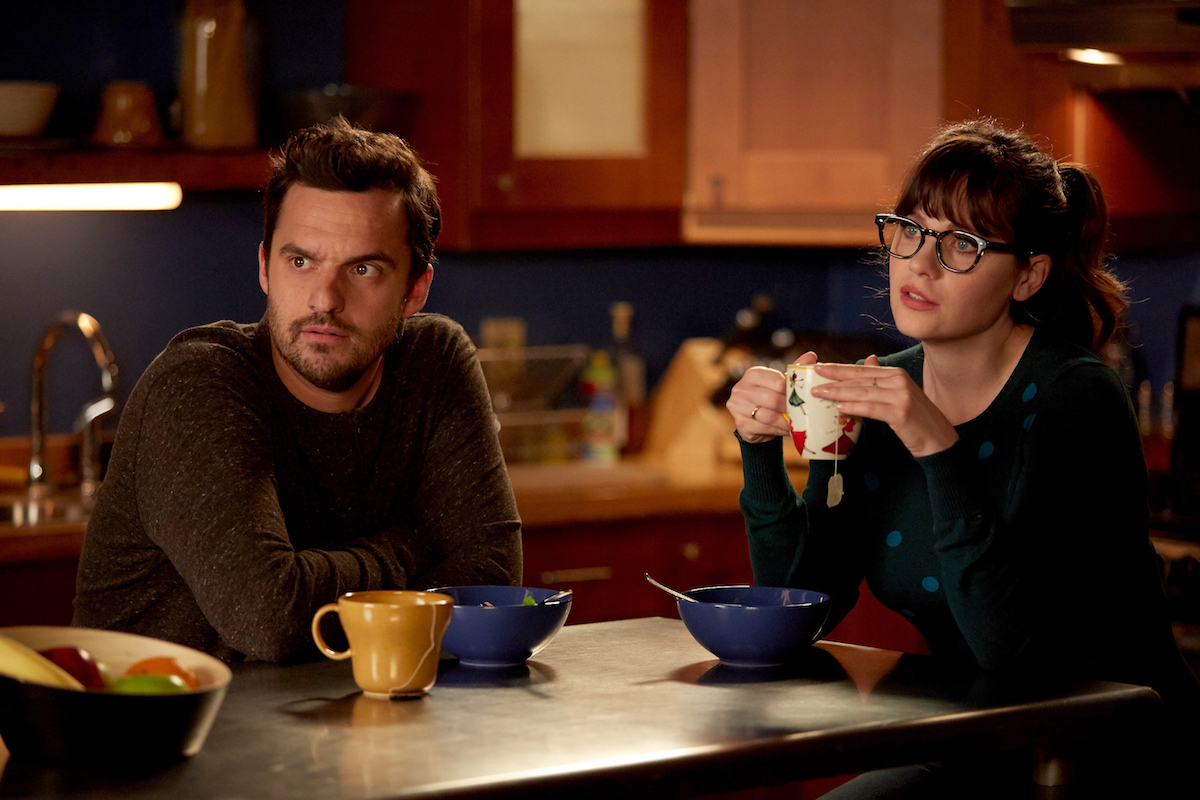 Jake Johnson and Zooey Deschanel in New Girl. They are sitting at a dining table.