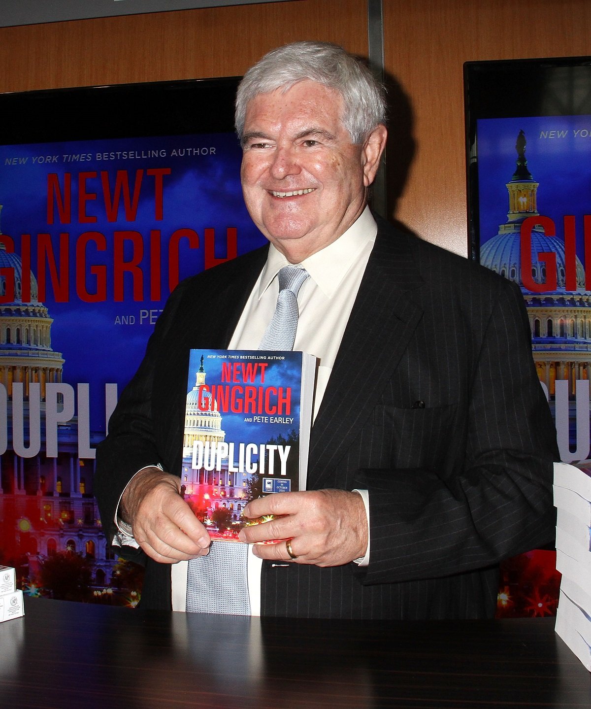 Newt Gingrich holding his book 'Duplicity' in 2015