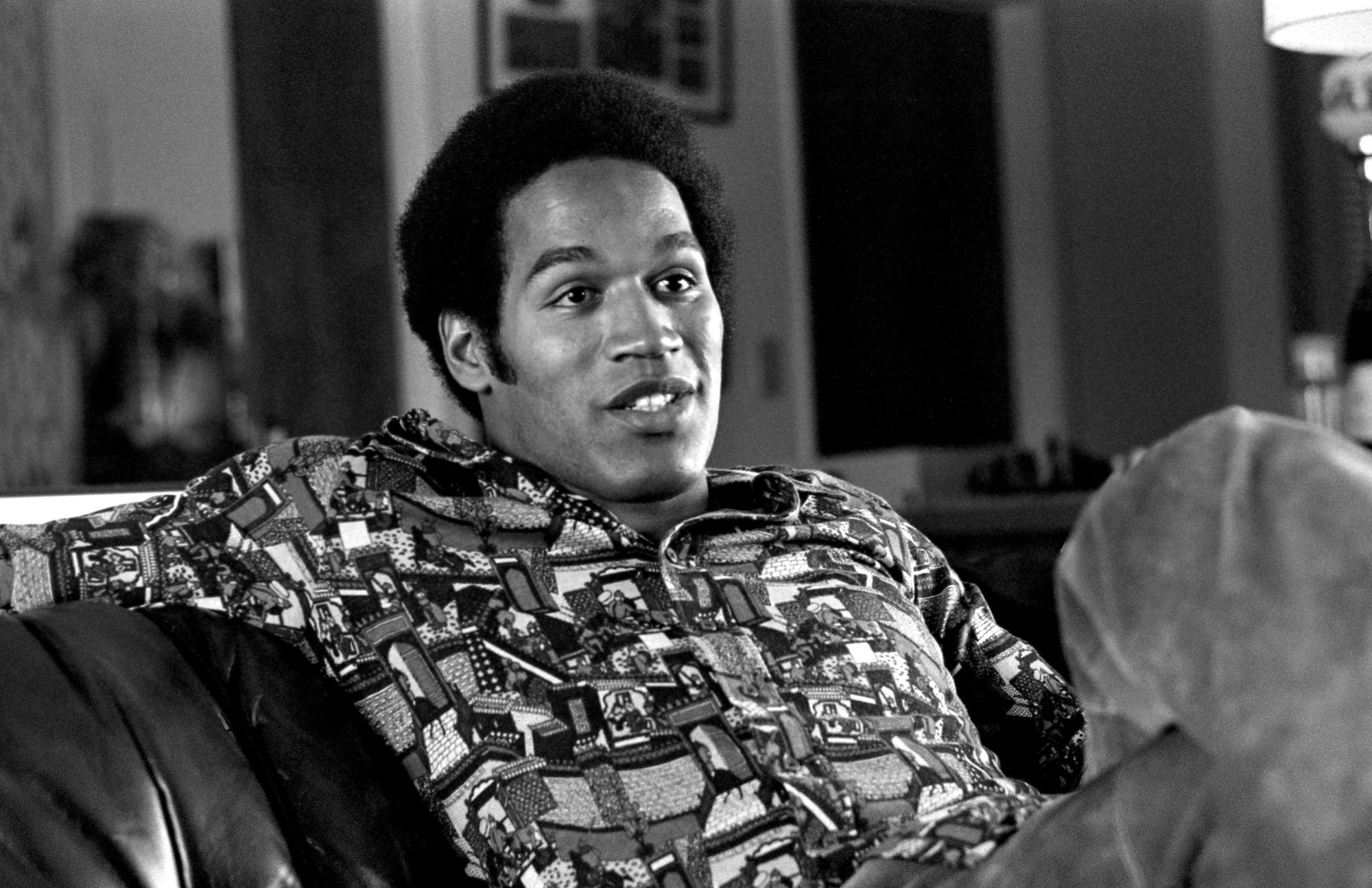 O.J. Simpson sitting on a couch, talking, in black and white