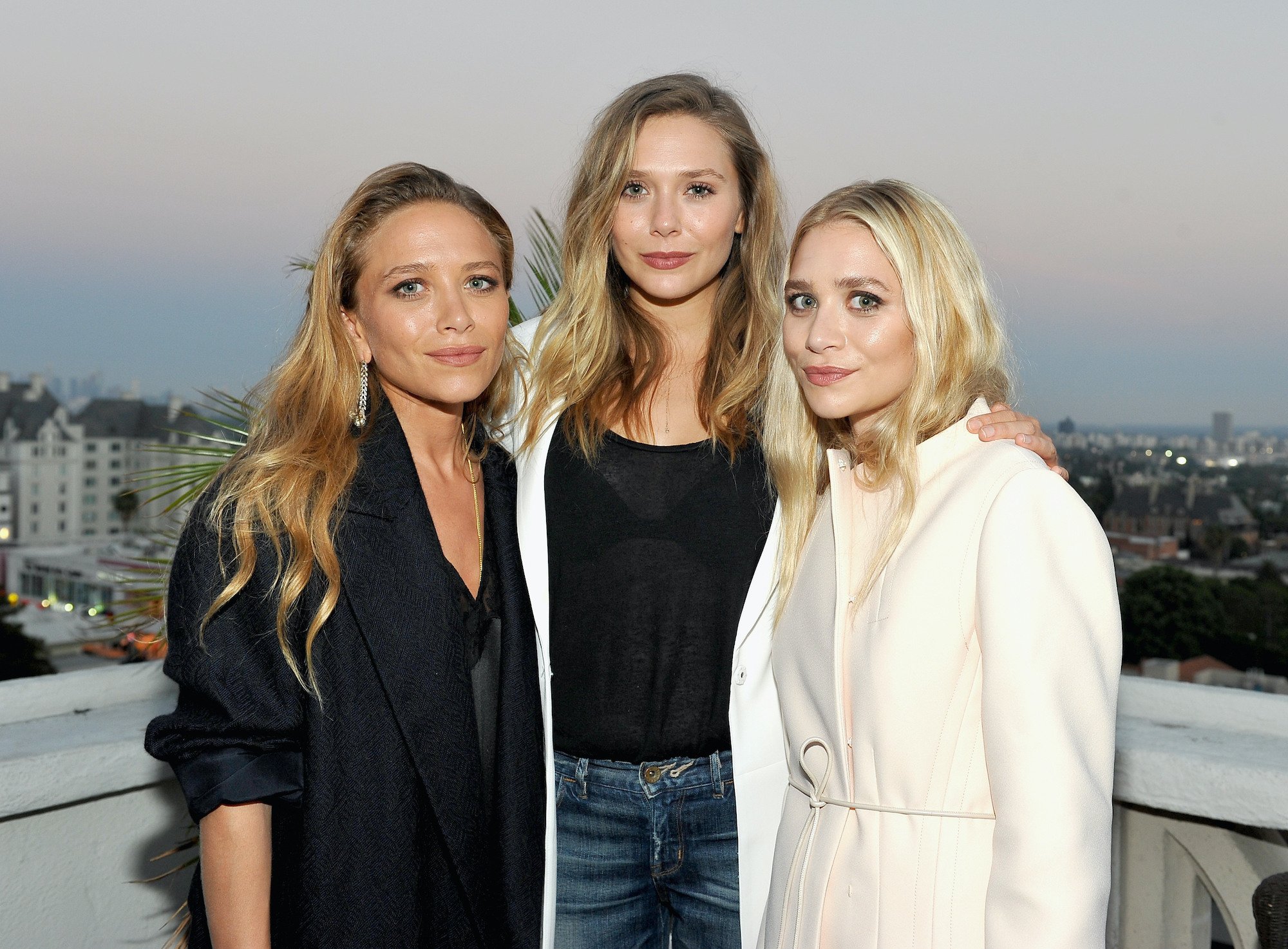 (L-R) Mary-Kate Olsen, Elizabeth Olsen and Ashley Olsen smiling in front of a cityscape