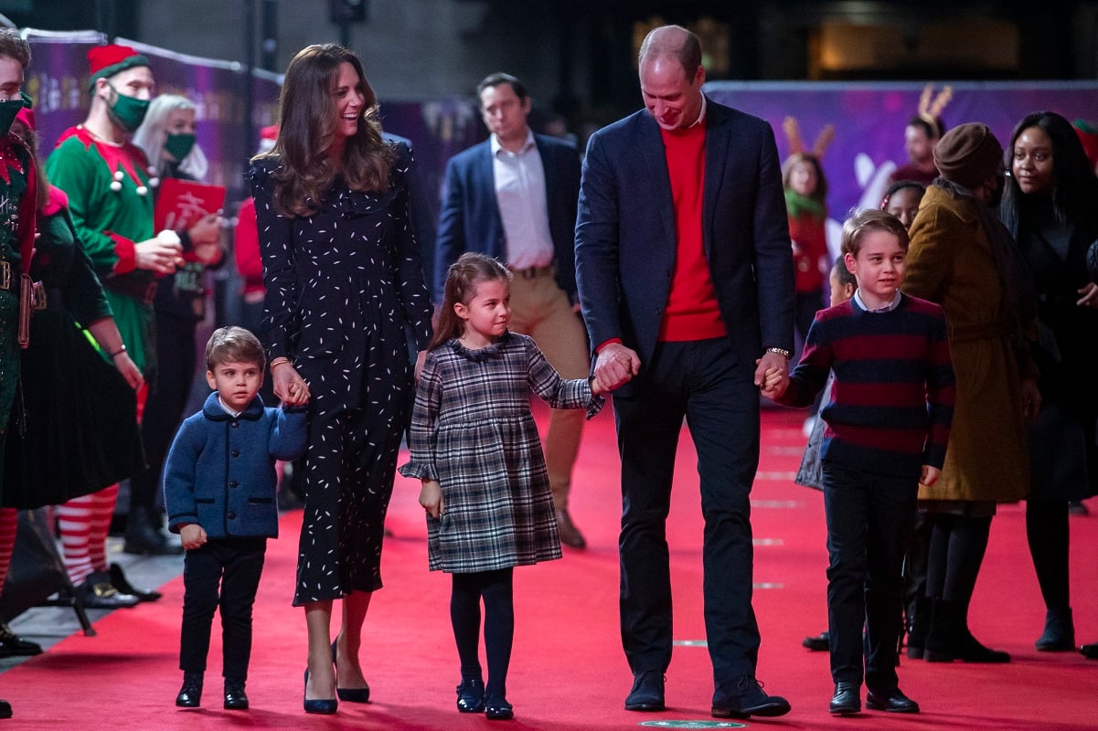 Prince William and Kate Middleton hold hands with their children as they walk the red carpet at a performance in London