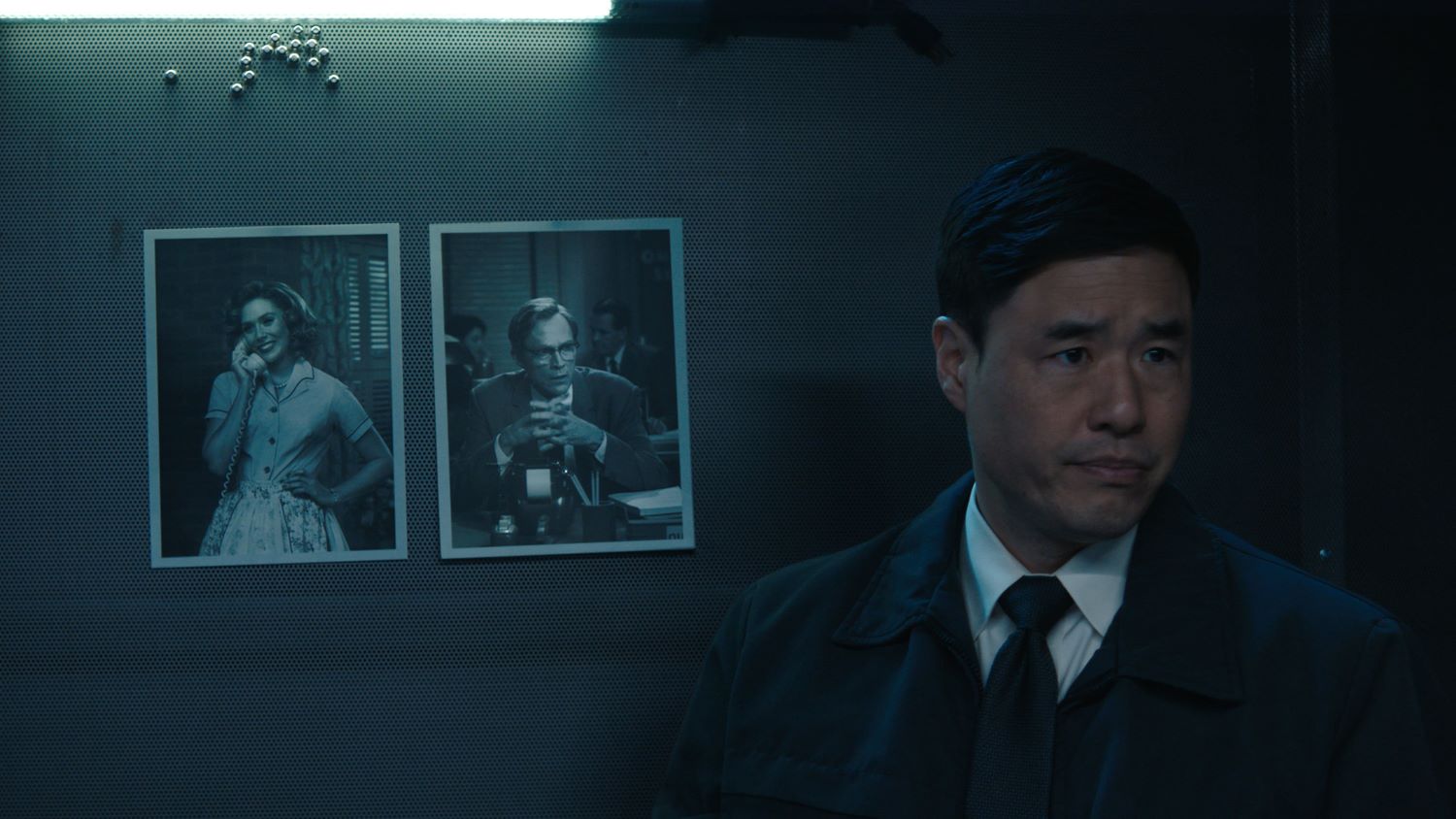 Randall Park in standing in front of photos of Wanda and Vision in 'WandaVision'