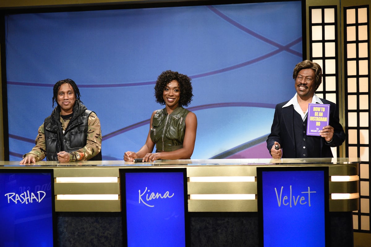 Chris Redd as Rashad, Ego Nwodim as Kiana, and host Eddie Murphy as Velvet Jones are on a gameshow set during the "Black Jeopardy" Sketch