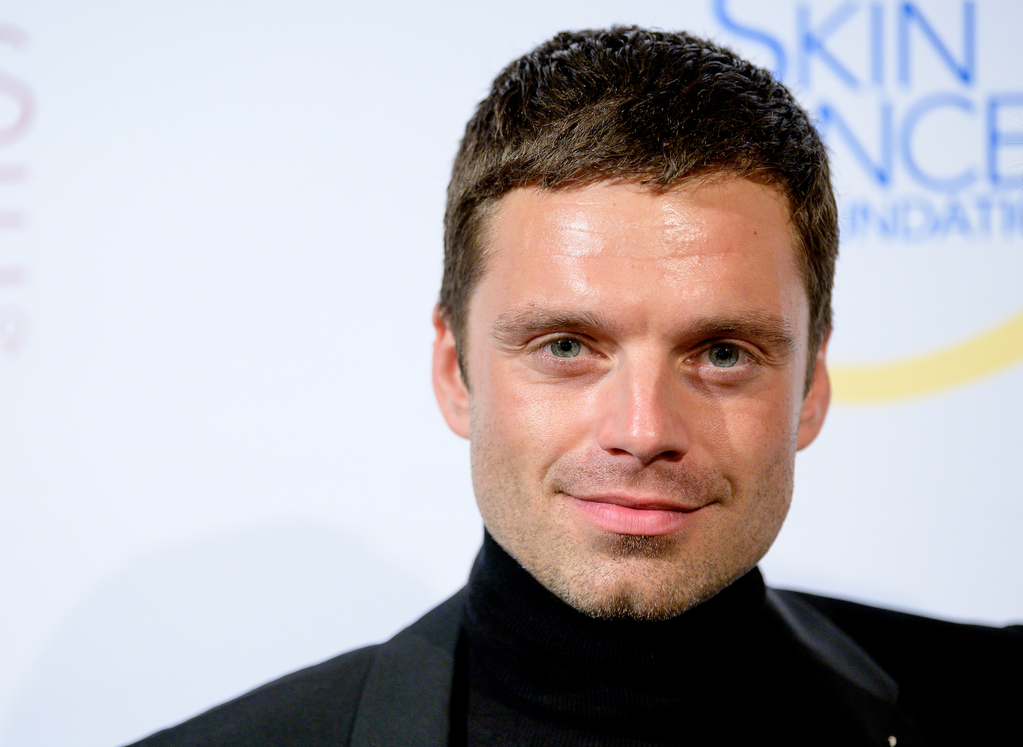 Sebastian Stan smiling in front of a white background