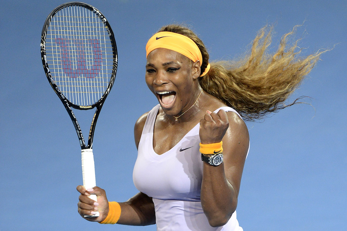 Serena Williams on the tennis court wearing white, a yellow headband and holding a tennis racket in her right hand.