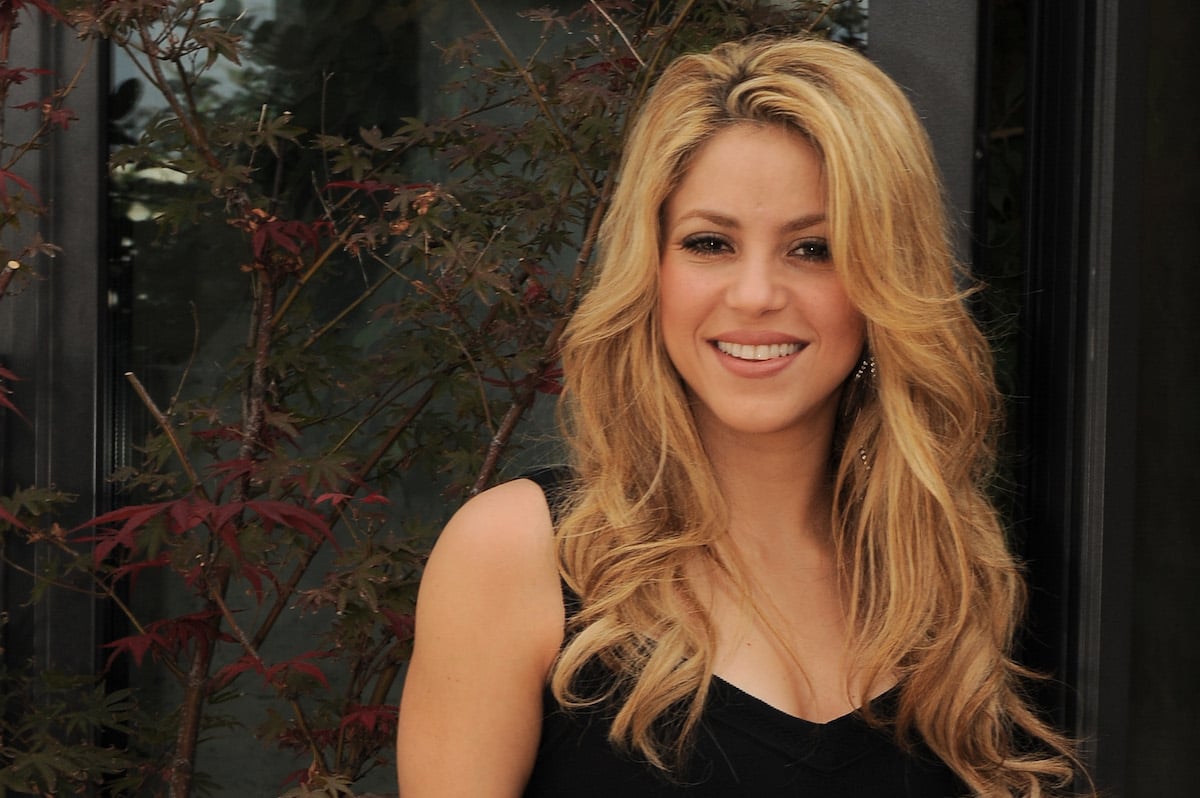 Shakira smiling at the camera with her hair down, wearing a black tank top.