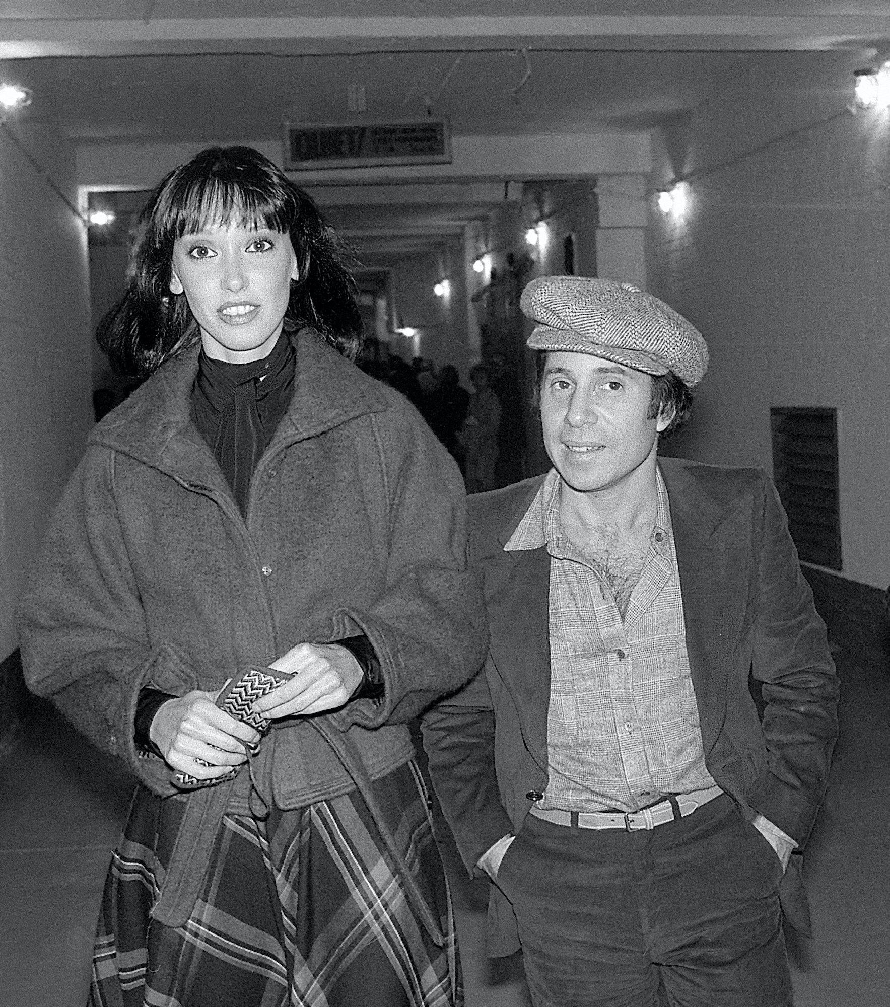 (L-R) Shelley Duvall and Paul Simon, walking down a hall, in black and white
