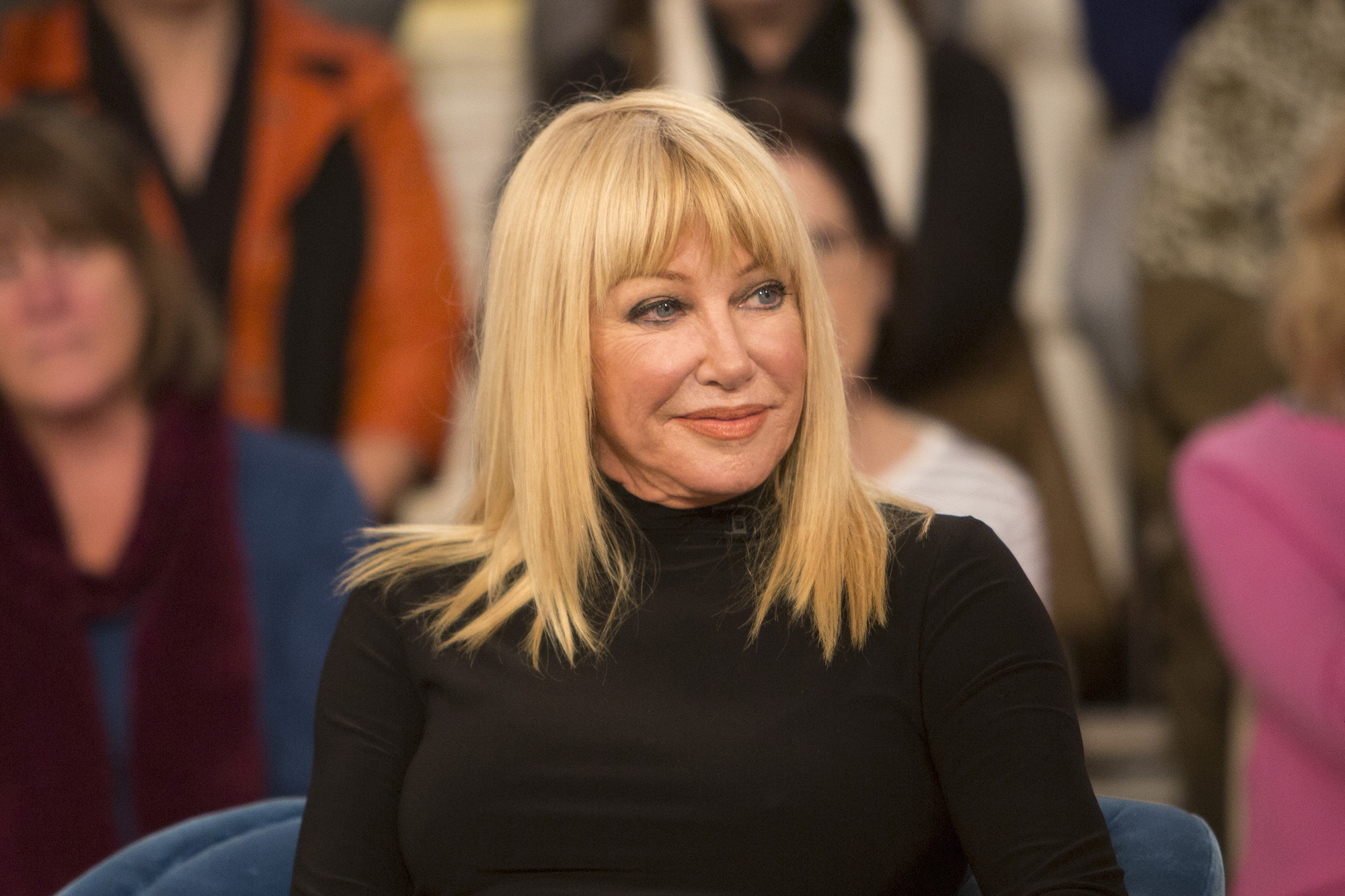 Suzanne Somers smiling, seated in front of a blurred audience