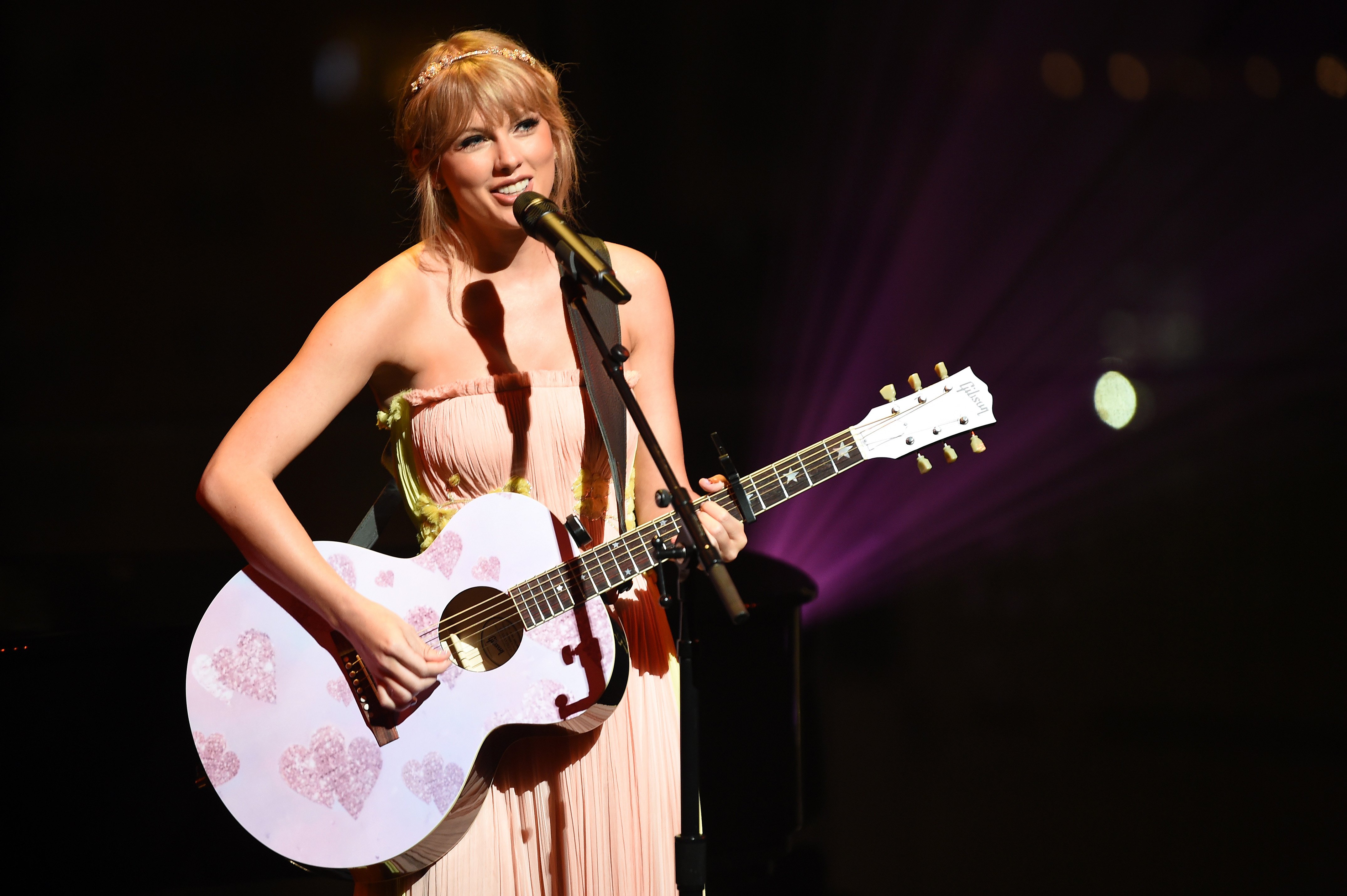 Taylor Swift holding a guitar with hearts on it as she performs at the Time 100 Gala in 2019