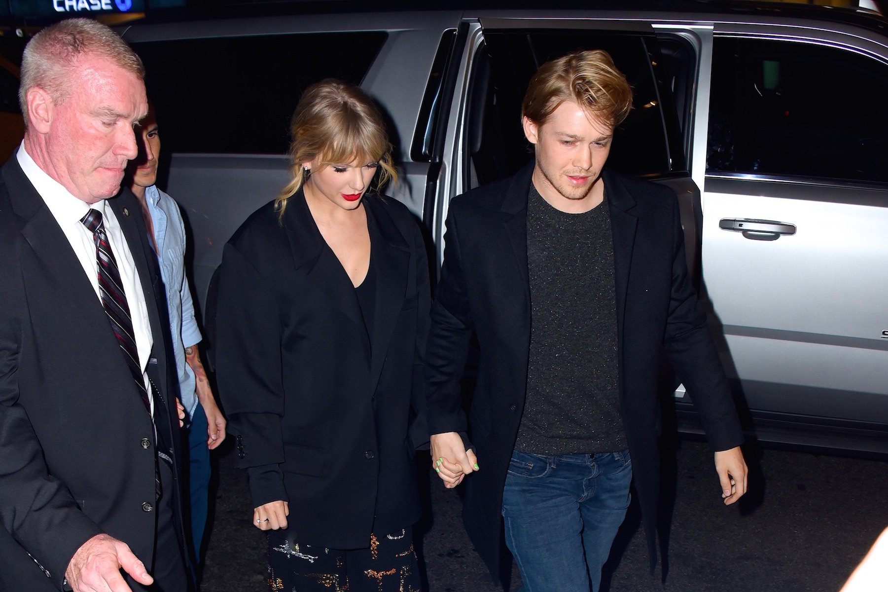 Taylor Swift and Joe Alwyn walking hand in hand away from a camera