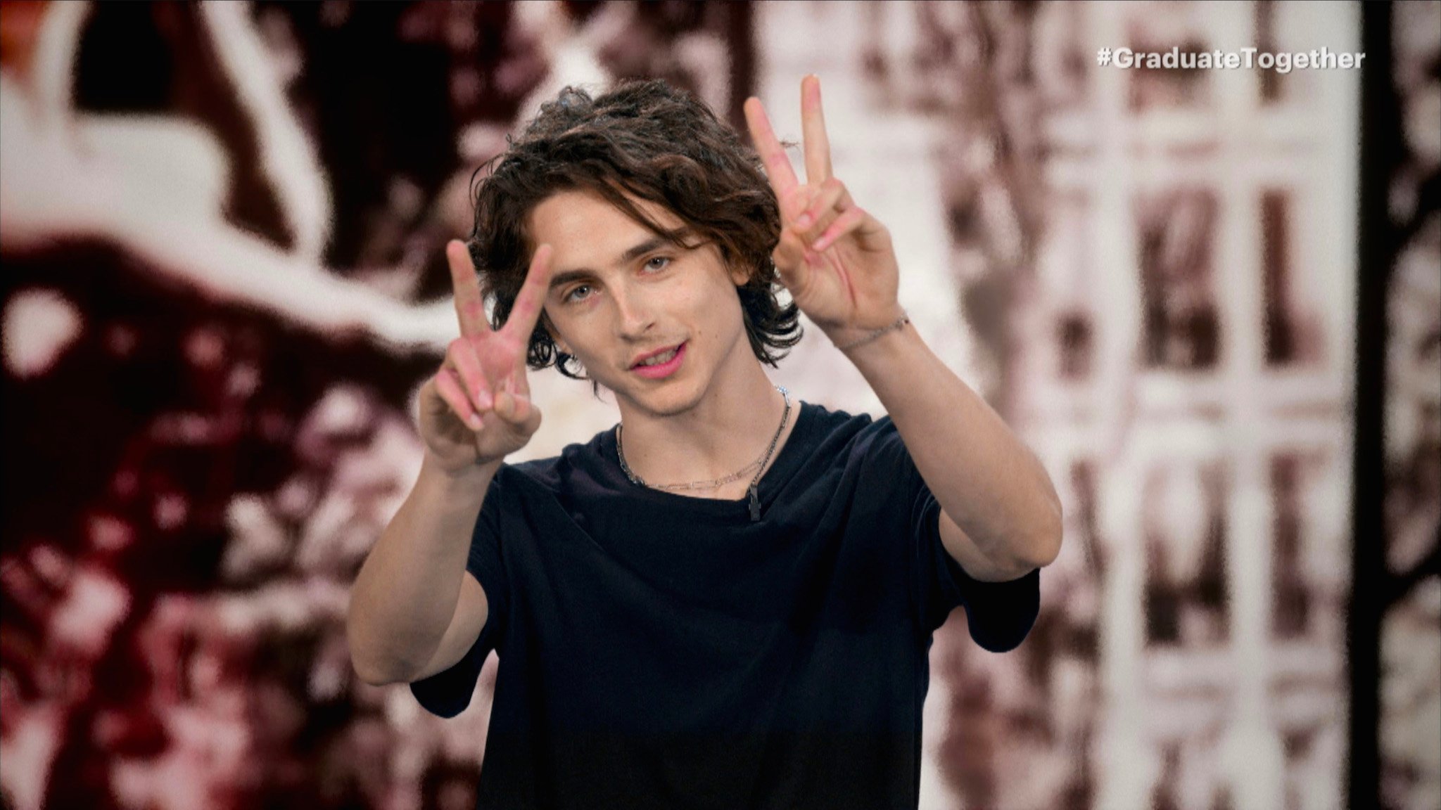 Timothée Chalamet holding up his hands with peace sign fingers