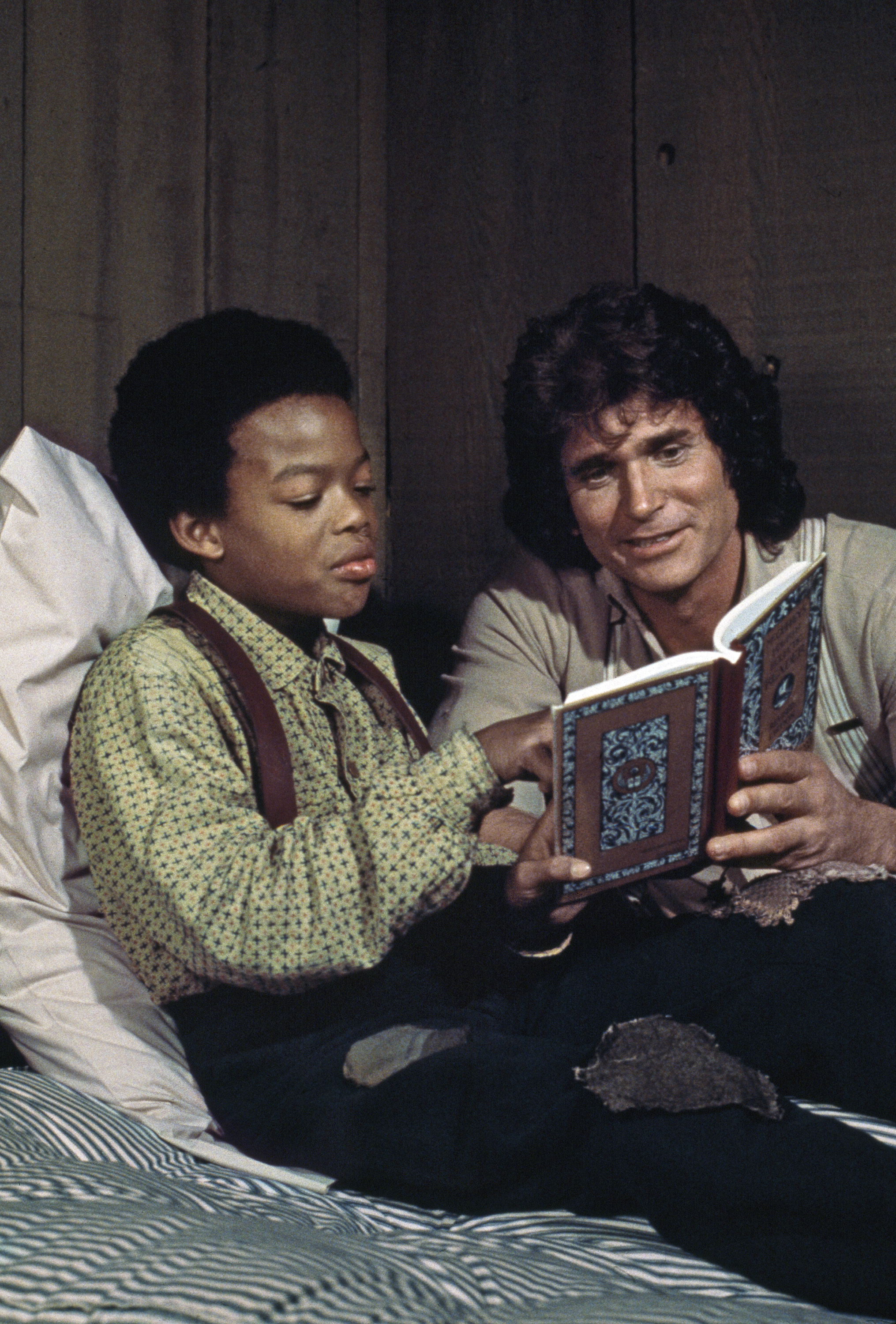 Michael Landon as Charles Ingalls reads a book to Todd Bridges as Solomon in an episode of Little House on the Prairie