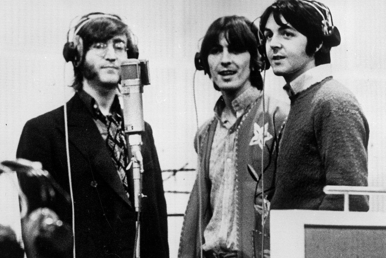 The Beatles standing around a microphone in a recording studio