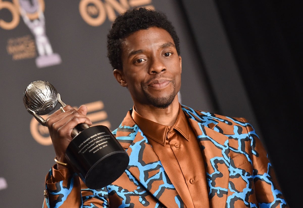 Chadwick Boseman holds his NAACP image award in a colorful suit.