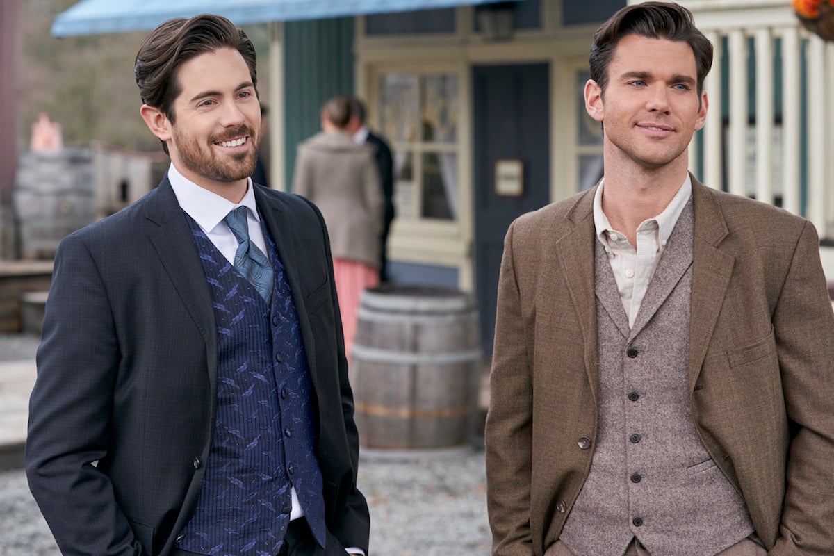 Chris McNally as Lucas, wearing a blue suit, and Kevin McGarry as Nathan, wearing brown jacket, standing next to each other on the street. 