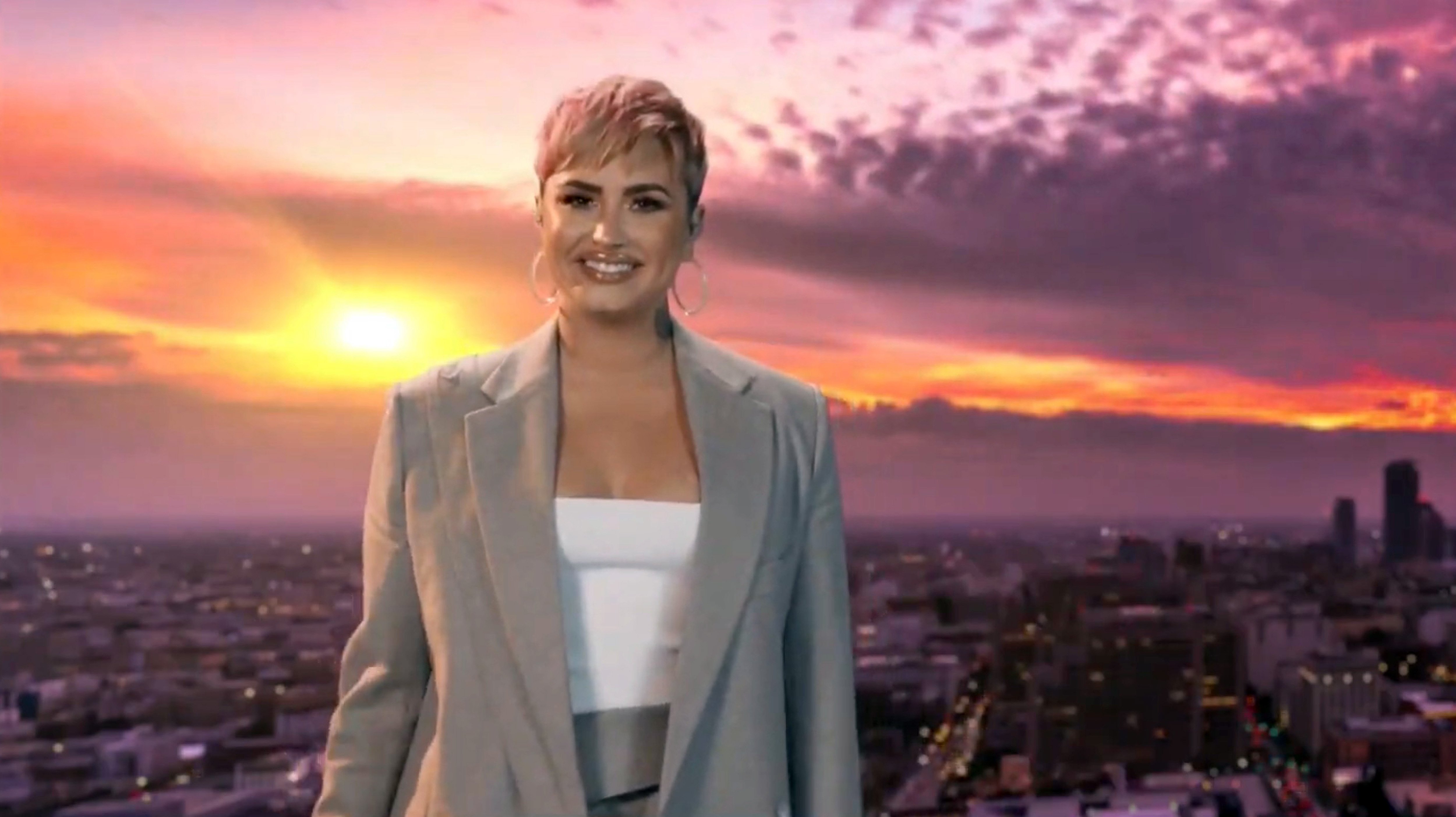 Demi Lovato smiling and standing in front of a sunset with her pink hair