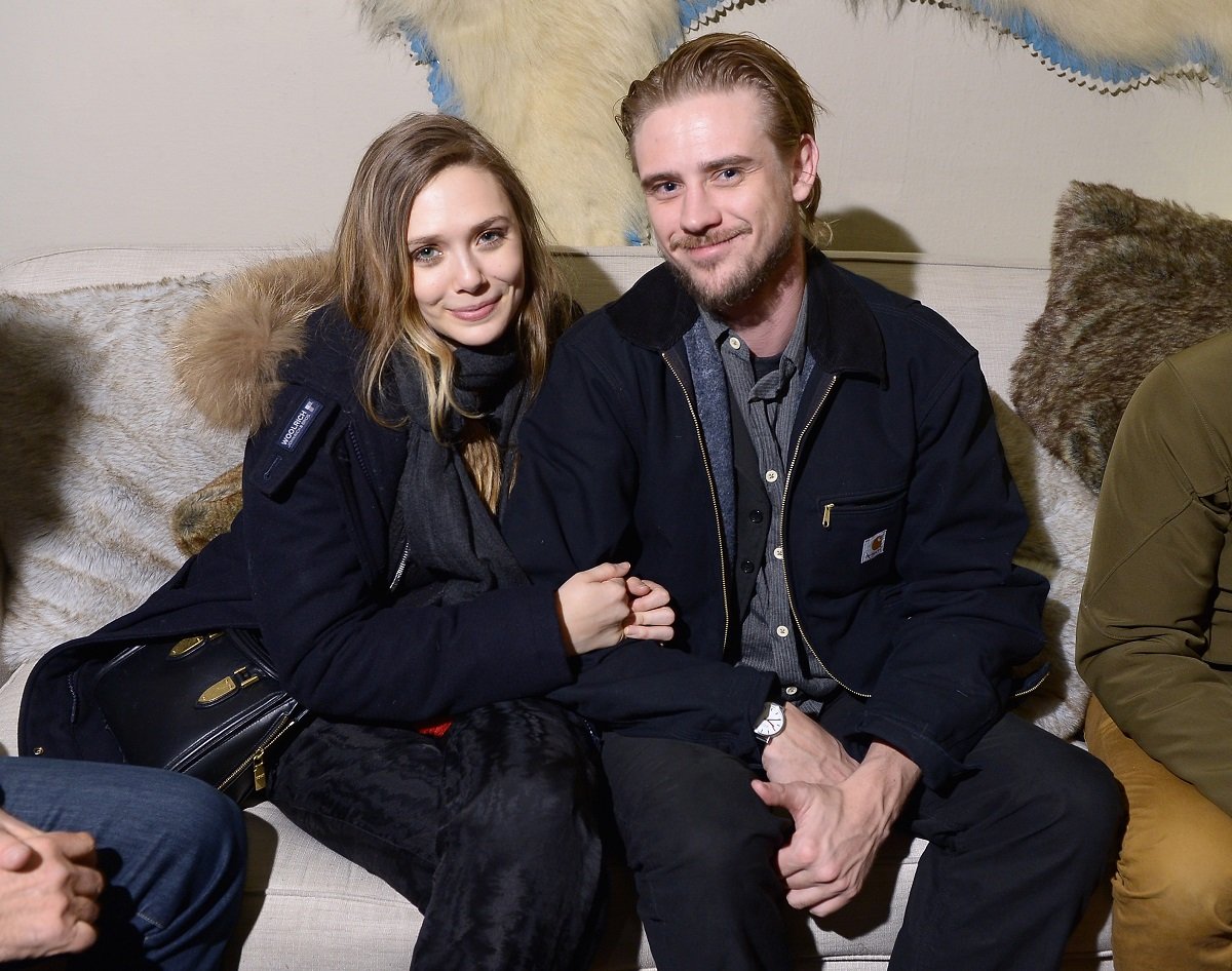 Elizabeth Olsen (L) holds Boyd Holbrook's arm while they sit on a couch.