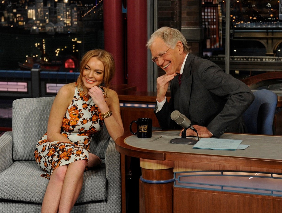 Lindsay Lohan (L) and David Letterman sitting in chairs and posing with their hands on their chins.