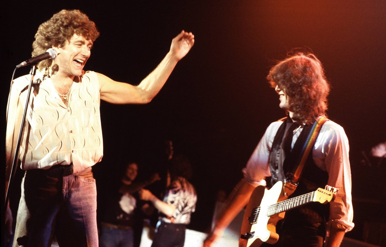 Robert Plant smiling and gesturing toward Jimmy Page on stage in 1983