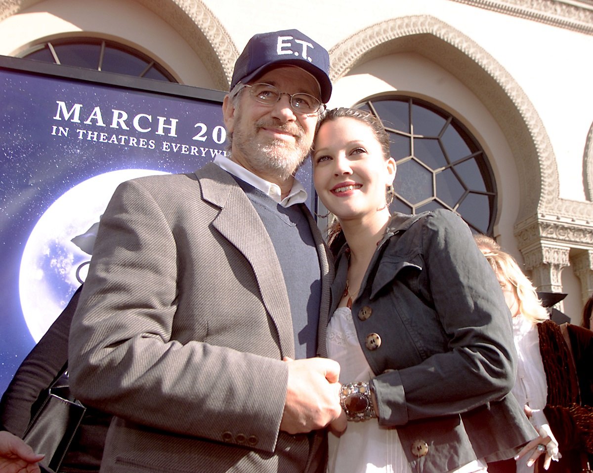 Steven Spielberg wearing an 'E.T.' baseball cap hold Drew Barrymore's hand