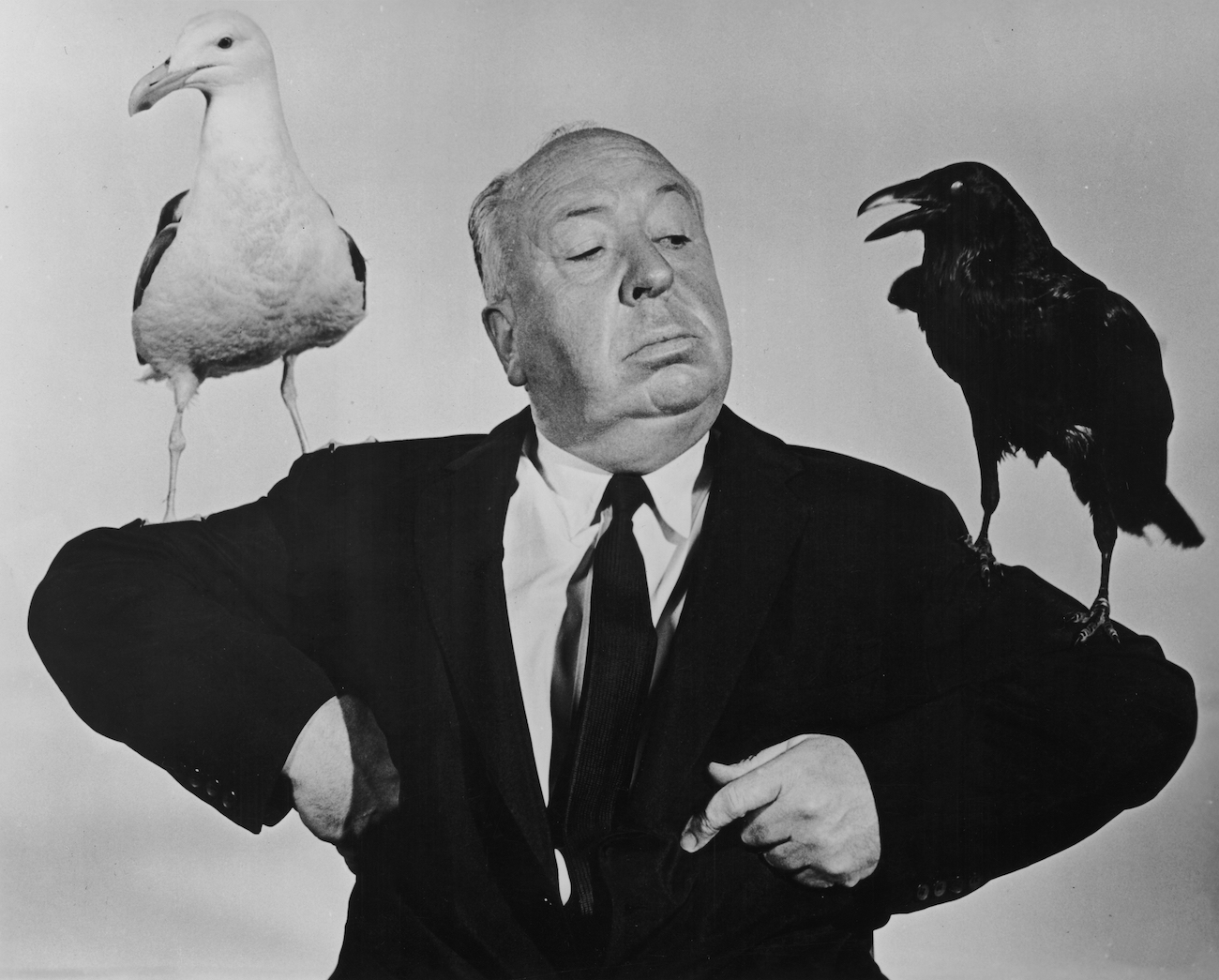Alfred Hitchcock (1899-1980) poses with a seagull and a raven perched on either arm in a promotional still for his film, 'The Birds'