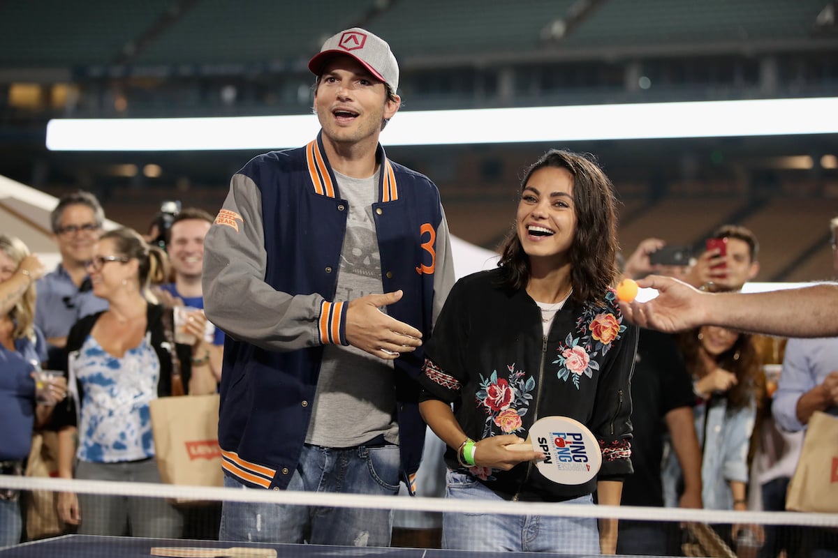 Ashton Kutcher and Mila Kunis stand next to each other at a ping pong table
