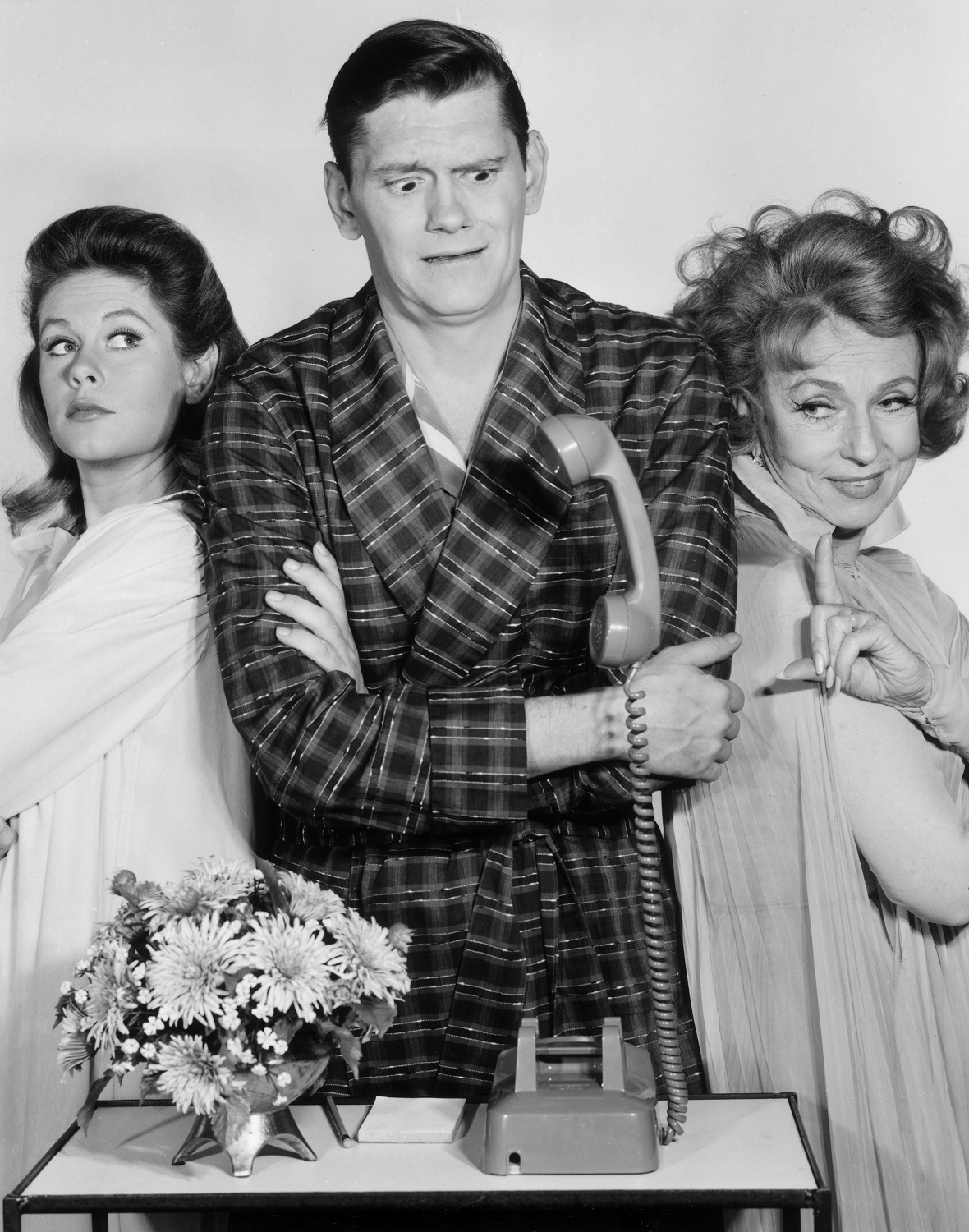 Elizabeth Montgomery, Dick York, and Agnes Moorehead, all wearing sleepwear, looking at a telephone with a levitating receiver, in a still from the television show, 'Bewitched'