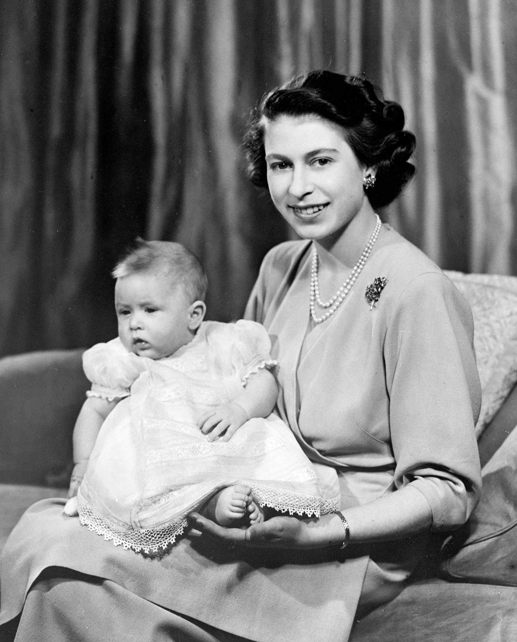 Black-and-white photo of Queen Elizabeth II holding Prince Charles when he was an infant