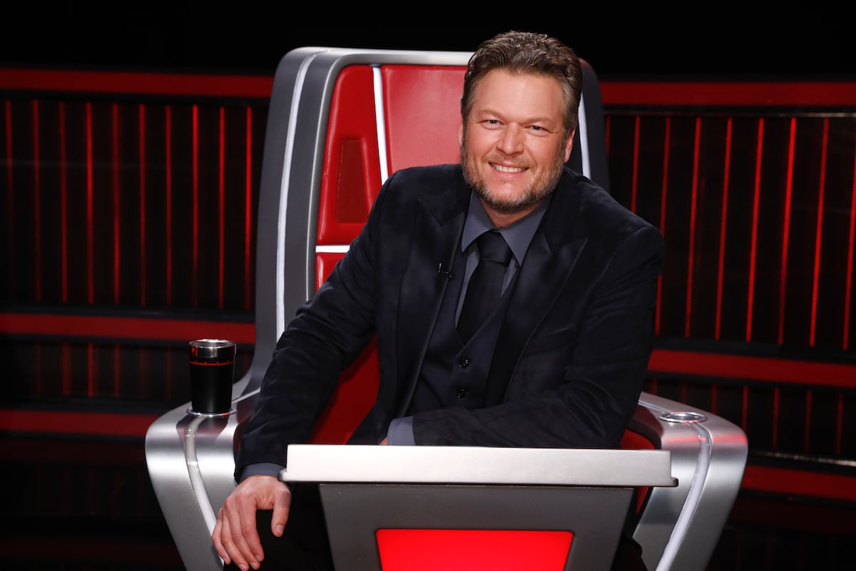 Blake Shelton sits in a chair wearing a black suit on 'The Voice'