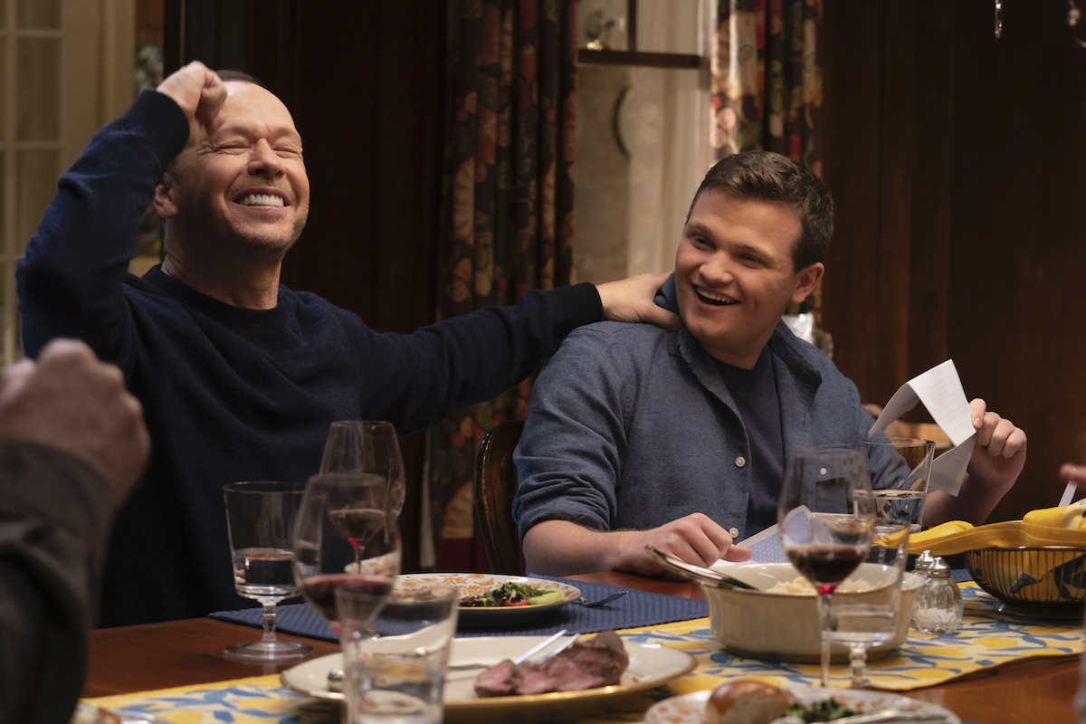 Donnie Wahlberg as Danny Reagan and Andrew Terraciano as Sean Reagan sit next to each other at the dinner table celebrating on 'Blue Bloods'