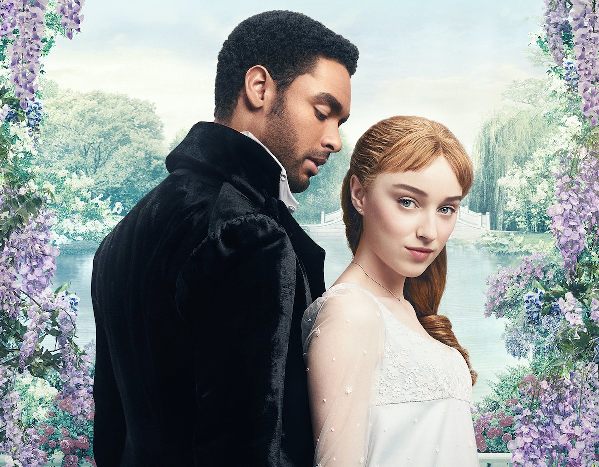 Regé Jean-Page and Phoebe Dynevor stand in front of a frame fo flowers in 'Bridgerton' | Netflix