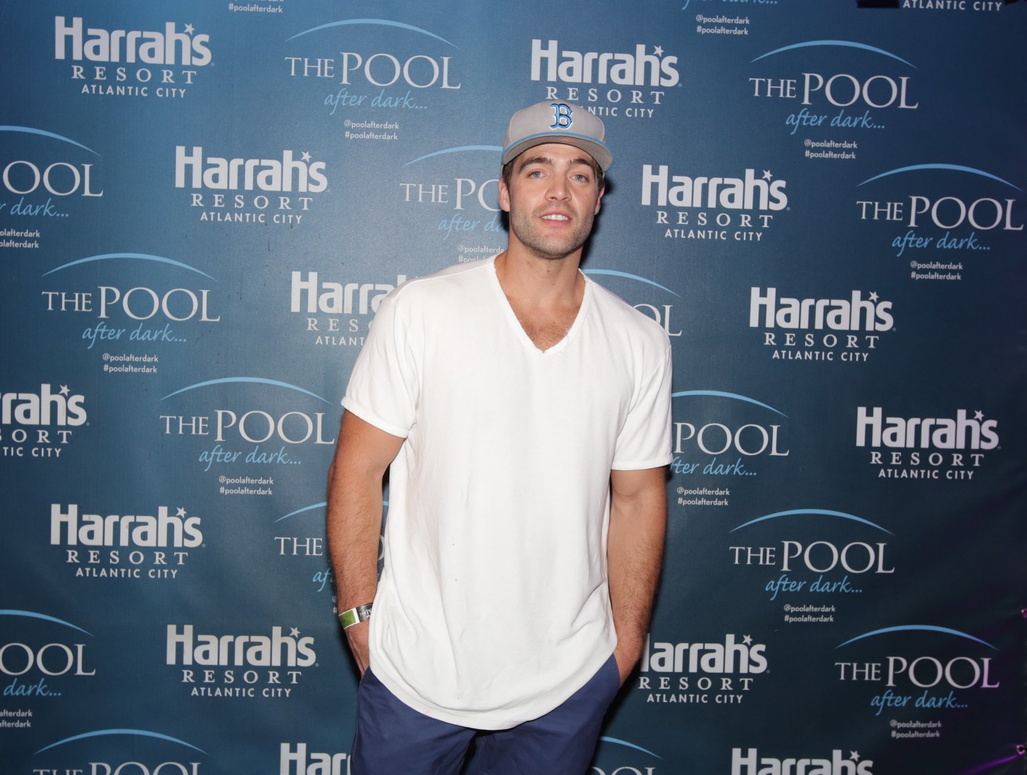 CT Tamburello from MTV's 'The Challenge' in a white T-shirt and a hat standing with hands in pockets for a camera