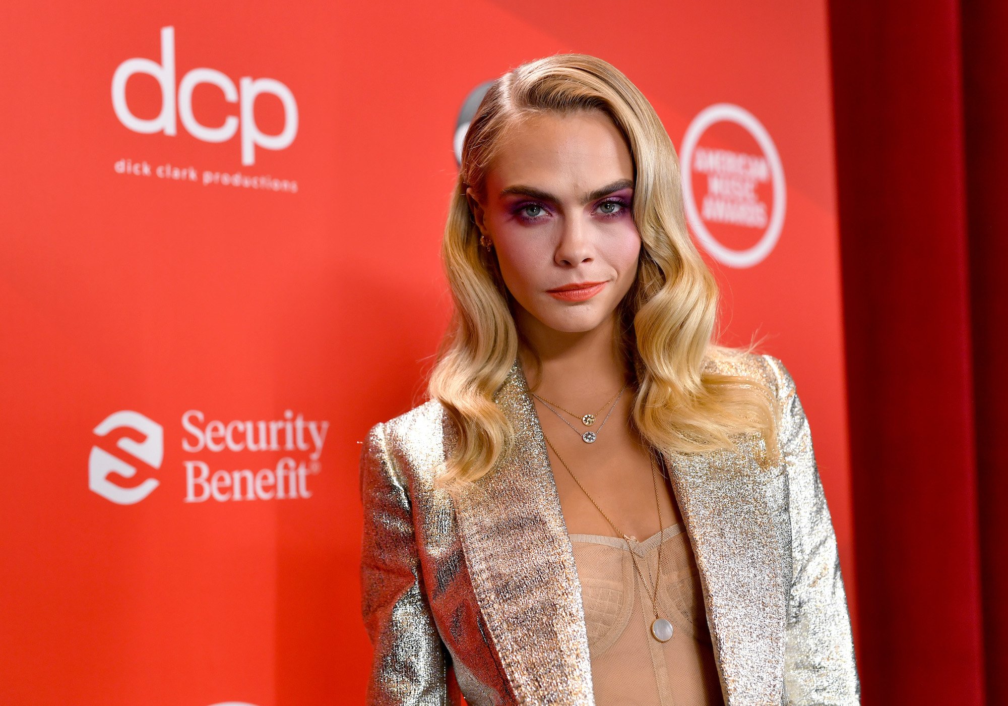 Cara Delevingne smiling in front of a red background