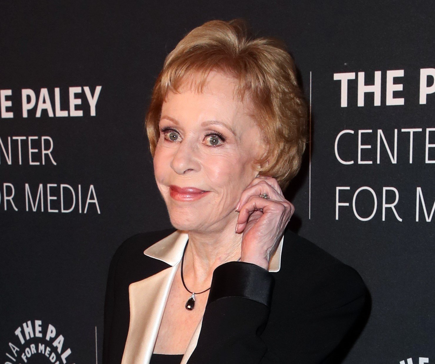 Carol Burnett smiles on red carpet and poses with her hand to her ear