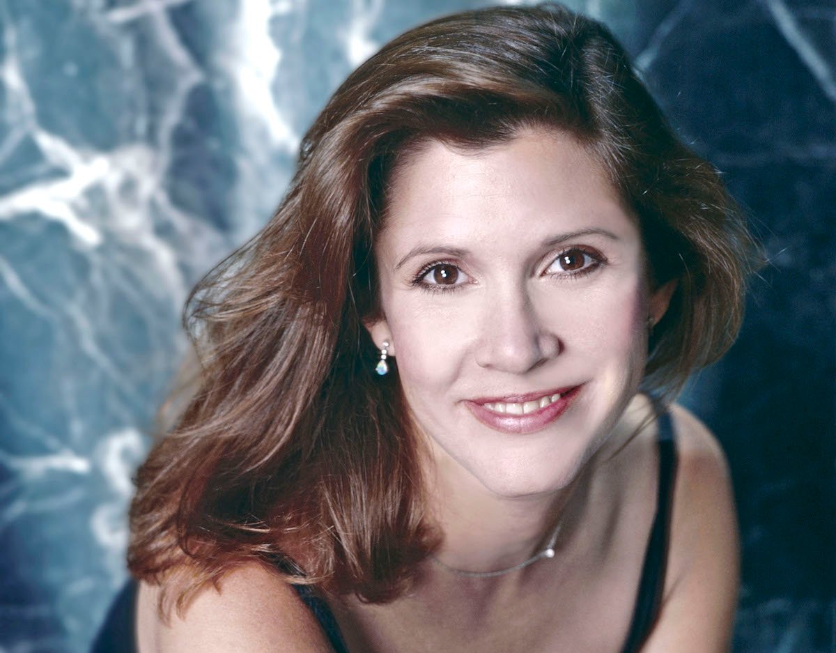 Young Carrie Fisher poses in front of a blue background and smiles for a portrait circa 1985 in Los Angeles, California | Aaron Rapoport/Corbis/Getty Images
