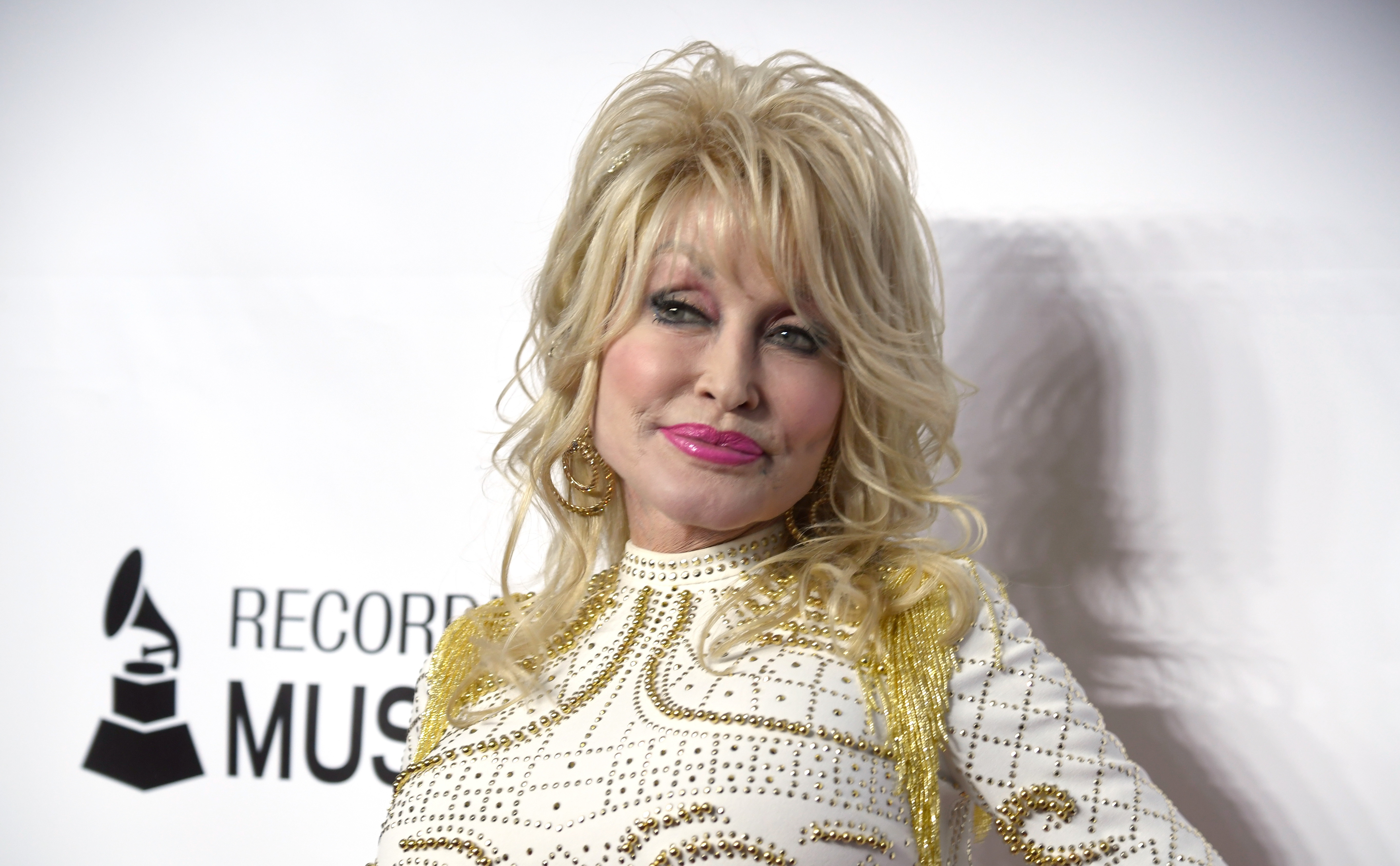 A close-up of Dolly Parton on the red carpet in a white and gold dress.