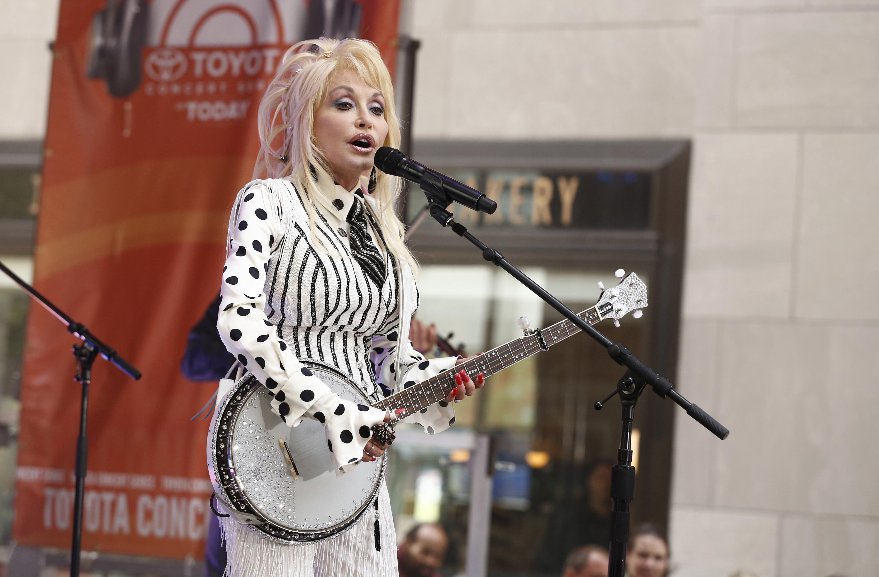 Dolly Parton performing on the 'Today' Show. She's singing into a microphone while playing a white banjo.