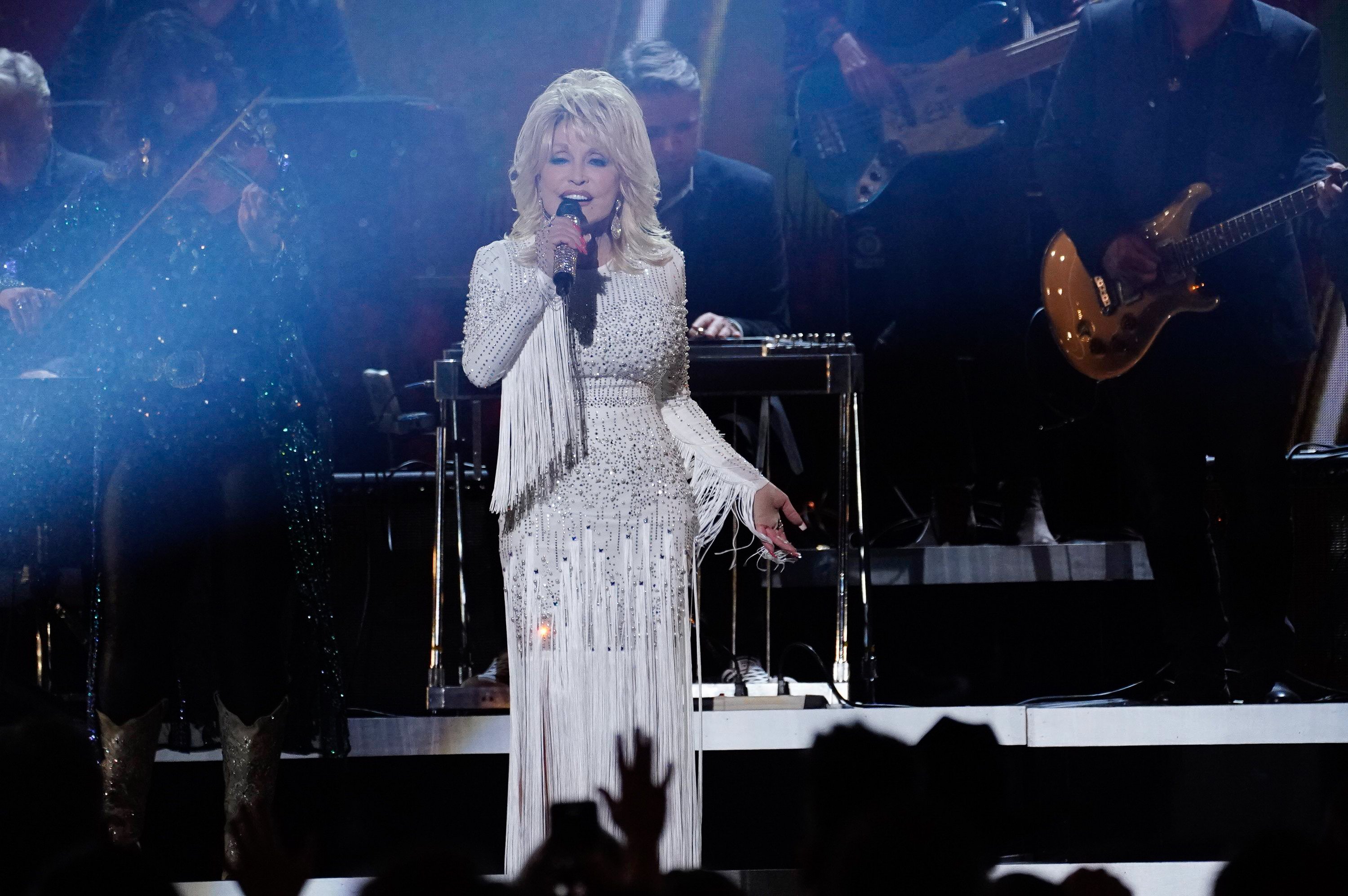 Dolly Parton performing on stage. She's in a white fringe dress.