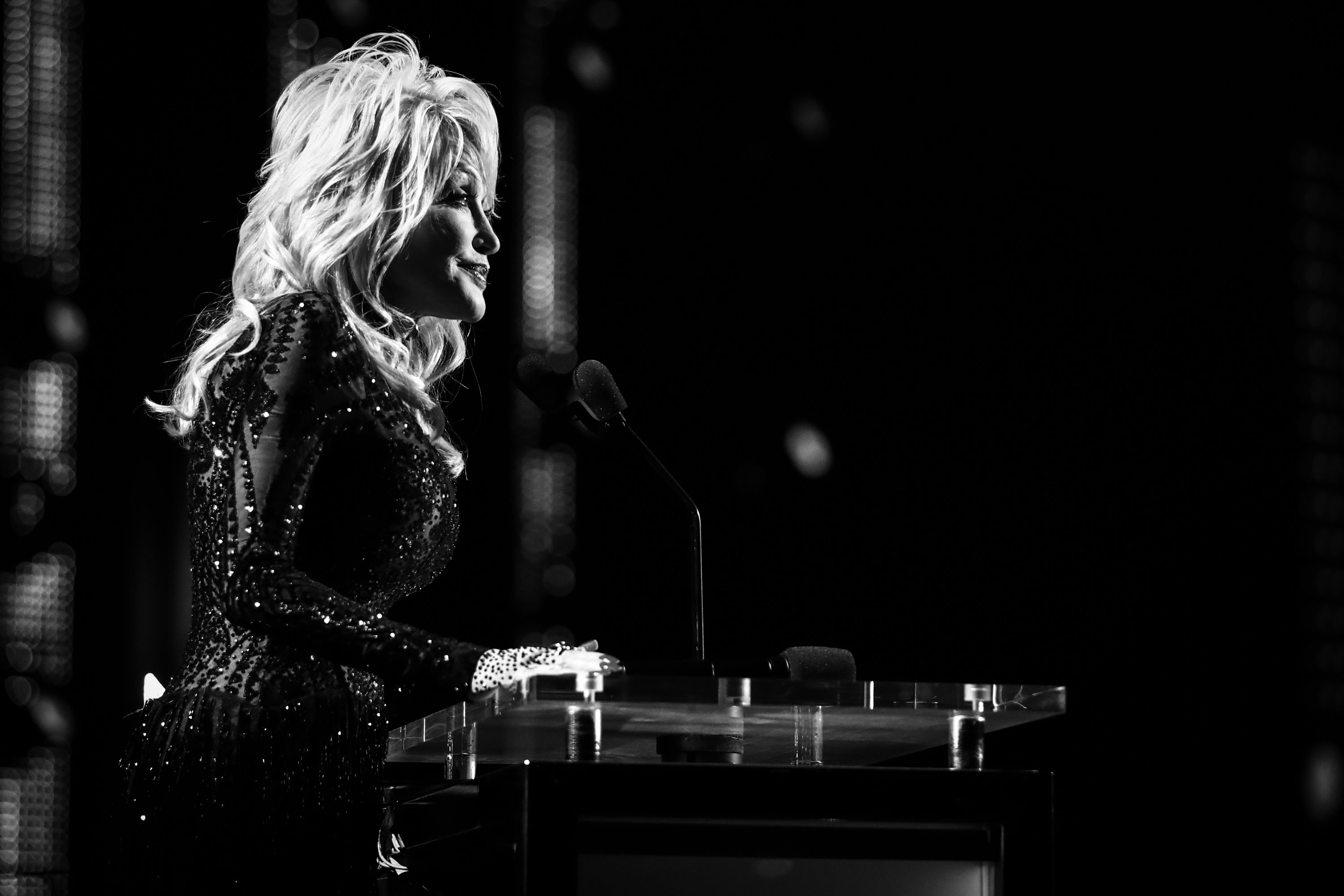 Dolly Parton photographed playing the piano on stage in black and white.