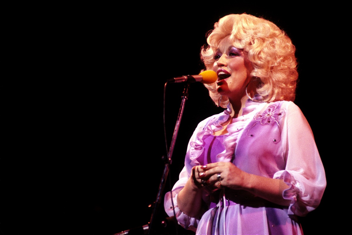 Dolly Parton in a pink dress singing at a microphone