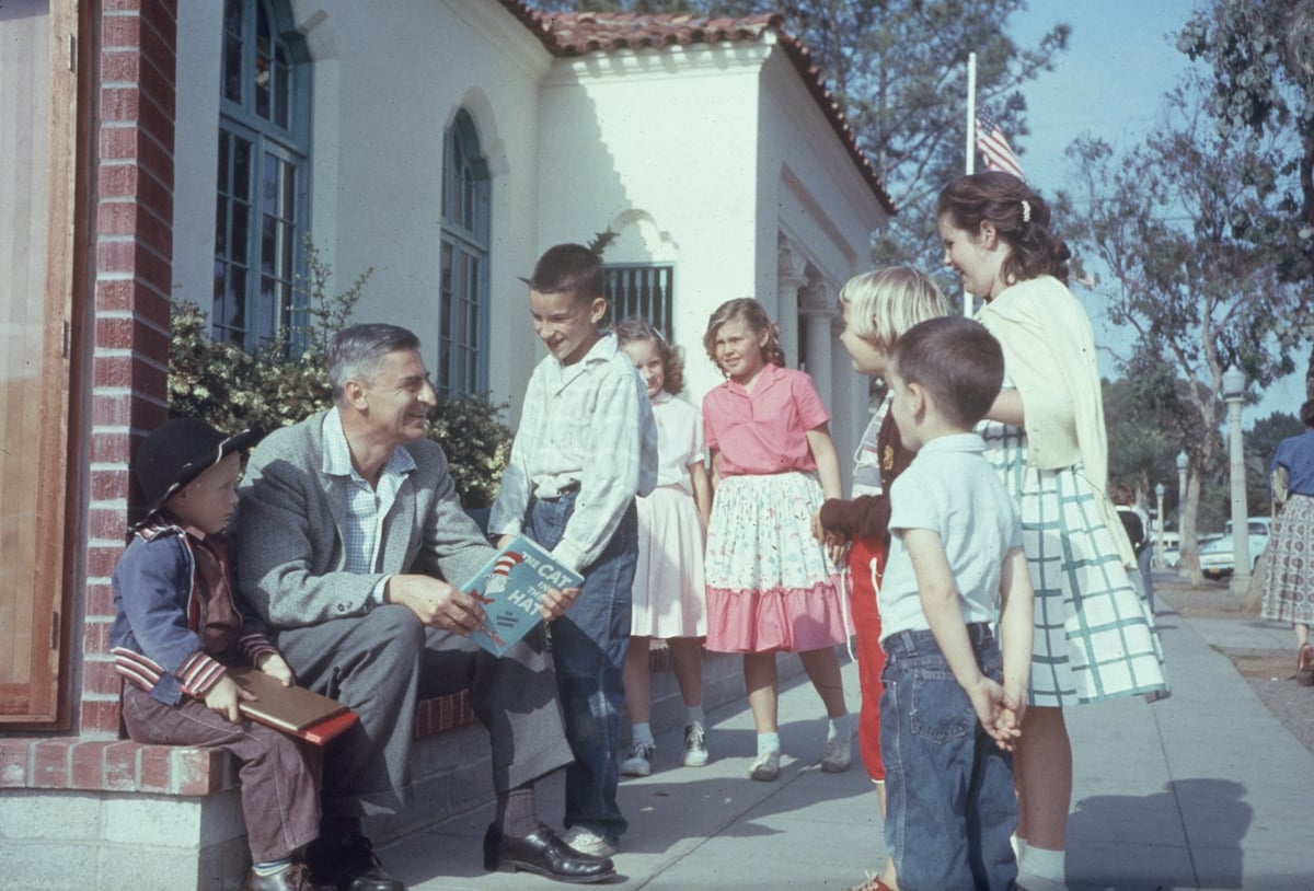 Dr. Seuss (Theodor Seuss Geisel, 1904 - 1991) sits outdoors talking with a group of children, holding a copy of his book, 'The Cat in the Hat', La Jolla, California, April 25, 1957