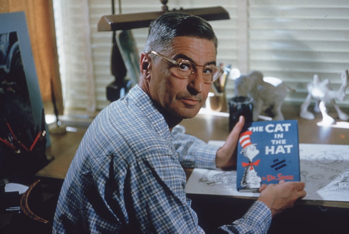 Dr. Seuss sits at his drafting table in his home office with a copy of his book The Cat in the Hat. | Gene Lester/Getty Images
