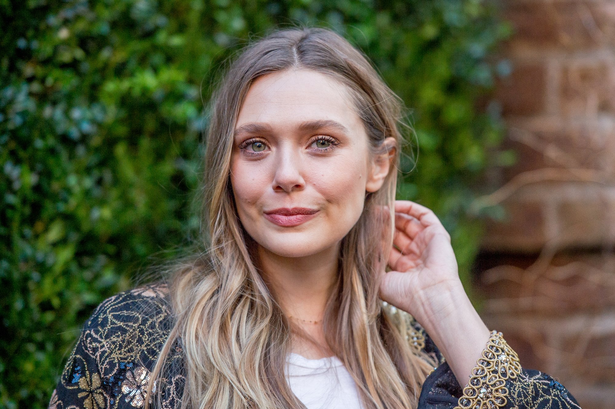 Elizabeth Olsen smiling in front of a brick wall