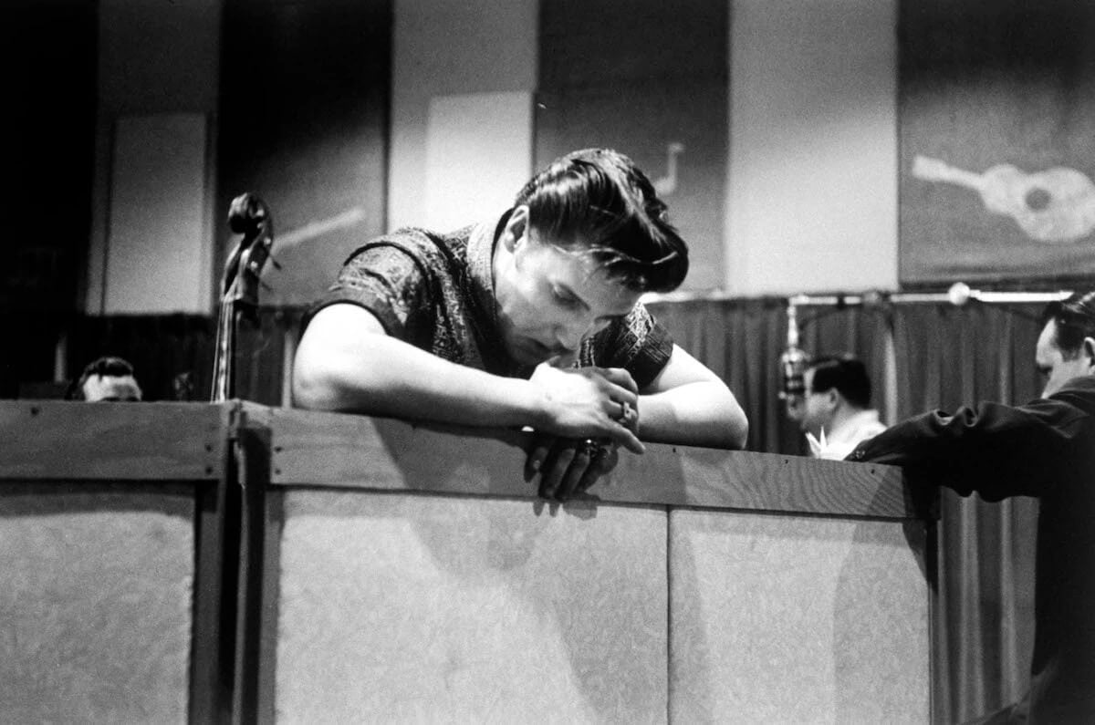Singer Elvis Presley, looking tired and somewhat dejected, leaning over the railing in a recording studio during a break from cutting a new record in 1956.