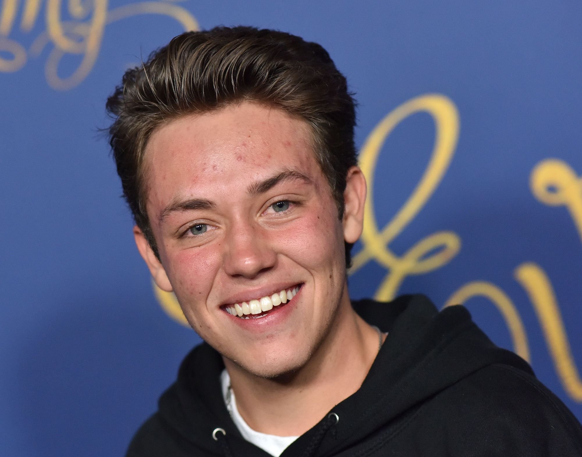 Ethan Cutkosky smiling in front of a blue background