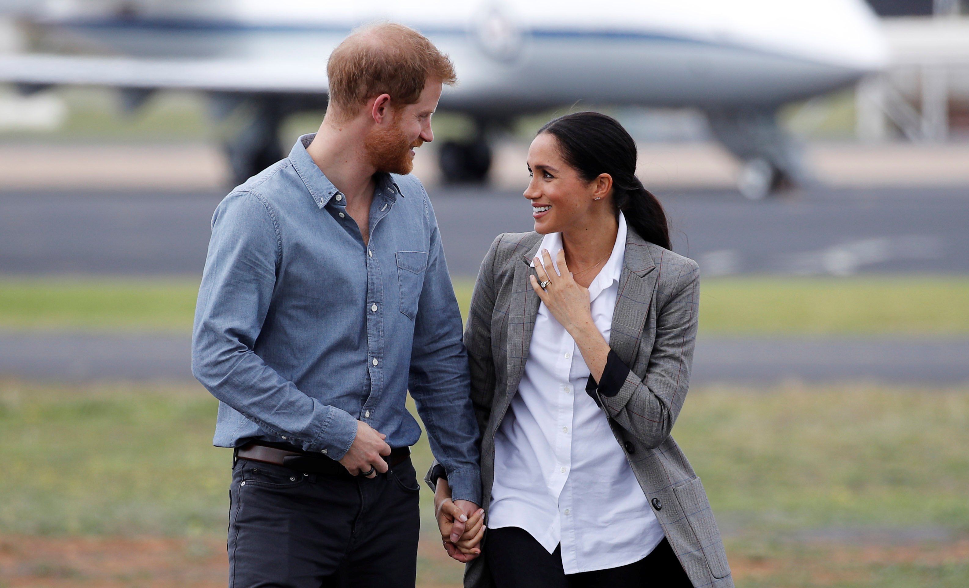 Prince Harry and Meghan Markle holding hands and smiling at each other as they arrive at Dubbo Airport